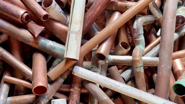 Overhead pile of copper plumbing pipes, elbows, couplings, soldered joints, and coated sections arranged edge to edge, creating industrial texture with worn surfaces and mixed oxidation