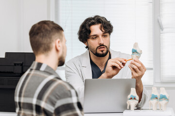 Fototapeta premium Orthopedic specialist presenting a knee joint model during a clinical consultation. Concept orthopedic examination, knee pain, musculoskeletal disorders, patient care, medical practice.