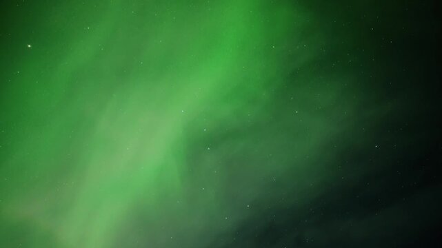Light green Aurora Norther lights dance across the stary sky as a few white clouds drift through the scene. Night sky time-lapse.

