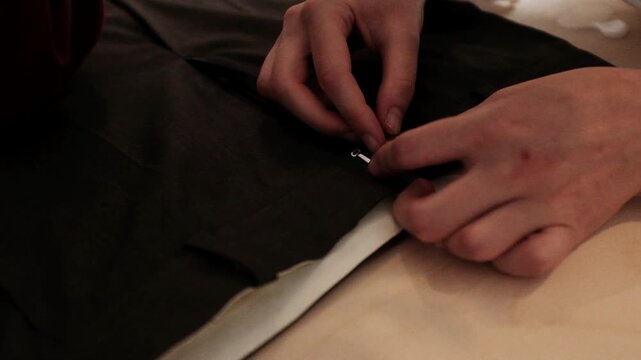 Close-up shot of a tailor carefully testing the zipper and aligning a metal clasp on the waistband of dark brown trousers. Apparel construction, custom tailoring tutorials, fashion design courses