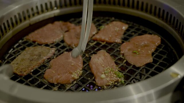 焼肉屋にて上カルビをトングで裏返しするシーン
