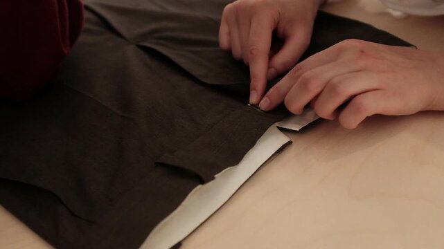 Close-up shot of a tailor carefully testing the zipper and aligning a metal clasp on the waistband of dark brown trousers. Apparel construction, custom tailoring tutorials, fashion design courses