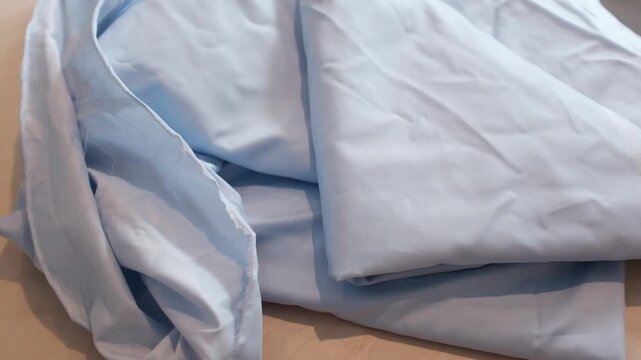 Heap of soft, light blue cotton fabric with slightly frayed raw edges. Sustainable textiles, material sourcing for fashion brands, home sewing basics, or clothing manufacturing tutorials