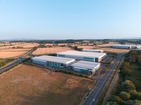 Aerial View of Modern Industrial Warehouse Complex in Green Countryside at Sunset &ndash; Commercial Buildings in Rural Setting