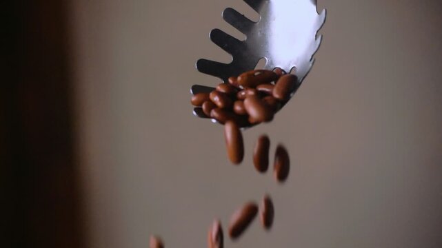 Close-up slow-motion footage of red kidney beans pouring from a large spoon. Ideal for themes of healthy eating, legumes, nutrition, food preparation, agriculture, and cooking ingredients.