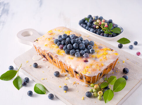 Homemade lemon blueberry loaf cake with homegrown blueberries  and lemon zest on a white cutting board; copy space