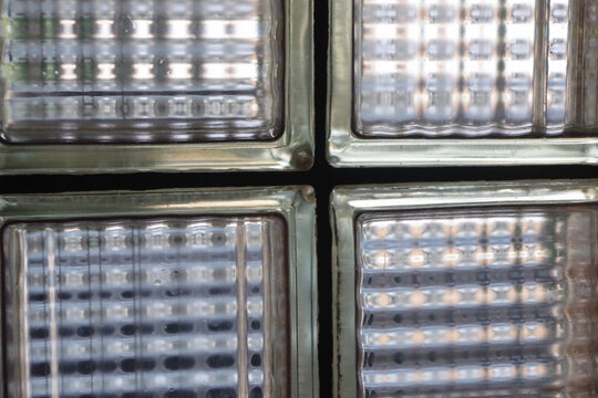 A close-up view of textured glass blocks arranged in a symmetrical grid, showcasing geometric patterns, soft reflections, and diffused light, creating an abstract background.