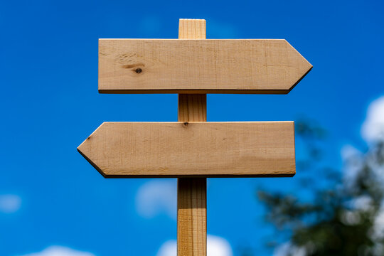 Blank wooden directional signpost with opposite arrows against blue sky, closeup. Empty wooden sign board with two arrows pointing left and right over bright blue sky background ready for copy space