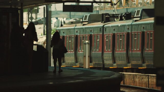 Woman walks along train platform as trains arrive and depart in busy city setting