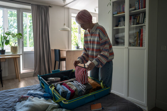 Organized mature woman traveler preparing for vacation trip and packing clothes in suitcase at home, preparation and planning for traveling, focused female accurately putting personal stuff in luggage