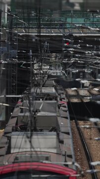 Train travels through a busy railway station in an urban setting during daylight hours