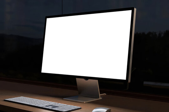 Side angle view of computer monitor with blank white screen mockup on wooden desk overlooking night landscape