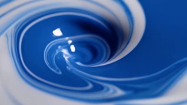 Blue paint is poured into white liquid, creating abstract swirling patterns.
