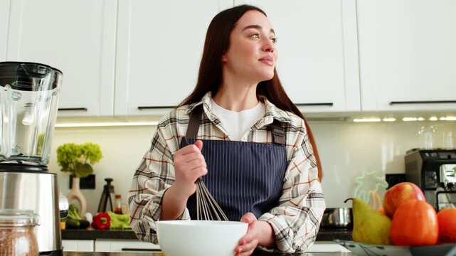 Young woman mixing batter with whisk in home kitchen for homemade meal prep healthy nutrition goals. Girl smiling during cooking practice creating fresh recipe for family dinner in apartment indoors.