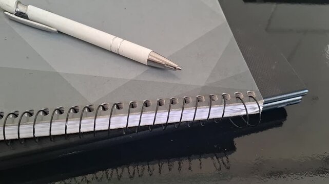 White ballpoint pen resting on grey notebook motion video footage