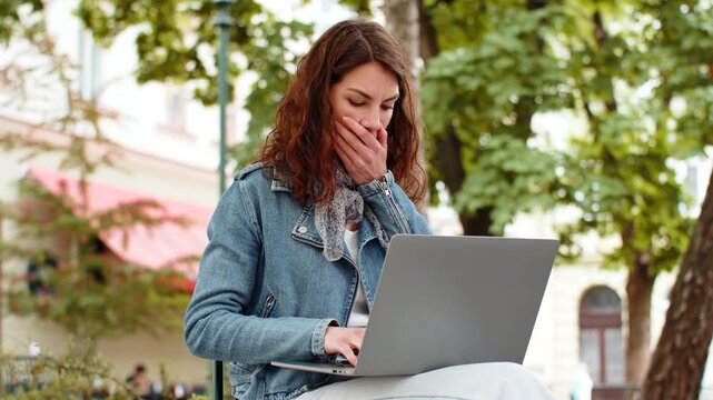 Young woman finding laptop error in city street park with shocked stressed mood at work. Girl tourist covering mouth outdoors after spotting mistake on computer during freelance work break near trees.