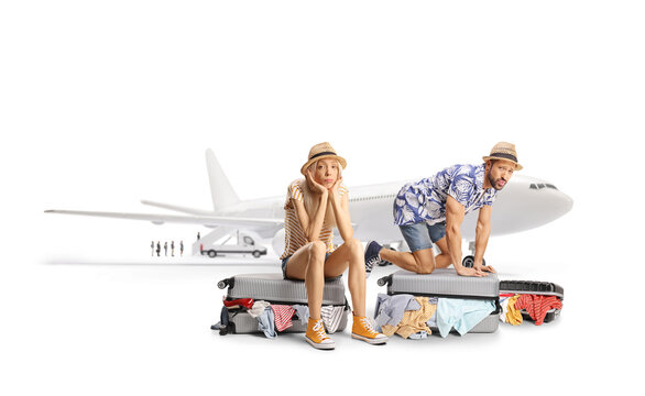 Stressed couple trying to close overpacked suitcase in front of a plane