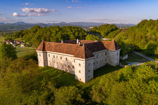 An aerial evening view of the Renaissance-era Krumperk Castle near Gorju&scaron;a, showcasing its four corner towers and red-tiled roof against a backdrop of the snow-dusted Kamnik&ndash;Savinja Alps at sunset