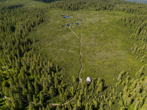 A high-angle aerial drone photograph capturing the expansive landscape of the Lovren&scaron;ka jezera peat bog on the Pohorje plateau, showcasing the wooden viewing tower at the forest edge