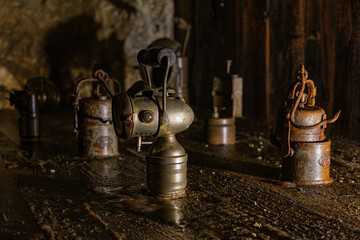 A historical museum display of antique miner carbide lamps (acetylene lamps) inside the Obir Dripstone Caves (Obir Tropfsteinhöhlen), showcased on an old wooden plank within a dark, mining gallery © erikzunec