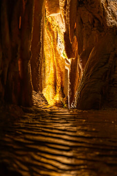 An interior vertical portrait photograph capturing an intimate, narrow passage inside the Obir Dripstone Caves (Obir Tropfsteinh&ouml;hlen), showcasing a glowing, translucent limestone drapery formation ba