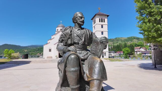 Andricgrad, Visegrad, Bosnia and Herzegovina - May 30, 2026: Statue of Ivo Andrić with the Church of Saint Lazar in the background