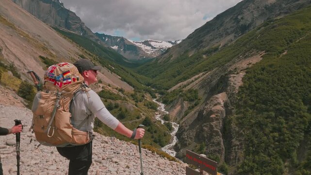 Woman hiker stands and enjoys valley view from windy pass viewpoint on the Torres del Paine W Trek, Patagonia, Chile