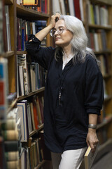 Woman with gray hair leaning by bookshelves reading a book © Валентина Хруслова