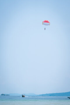 Parasailer soaring above Phu Quoc sea with colorful canopy and boat cutting through water