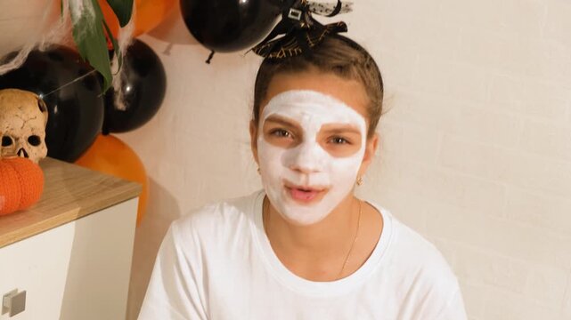 A cute teenage girl is getting ready for Halloween and doing face painting, with a skeleton painted on her face. October is a time of horror.