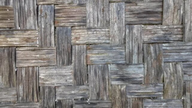 Close-up of weathered traditional bamboo woven wall texture with intricate pattern and aged gray wooden tones.