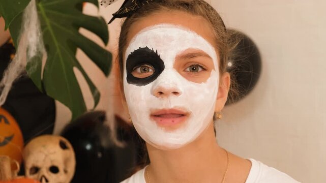 A cute teenage girl is getting ready for Halloween and doing face painting, with a skeleton painted on her face. October is a time of horror.