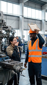 Diverse engineers laughing together beside milling machine in modern manufacturing plant