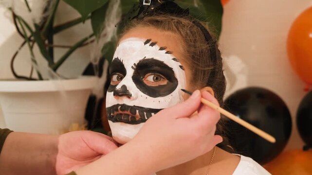 A cute teenage girl is getting ready for Halloween and doing face painting, with a skeleton painted on her face. October is a time of horror.