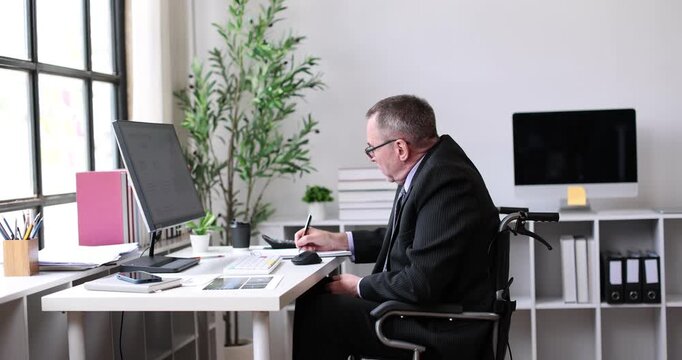 Man in wheelchair diligently analyzing digital business charts and data on a desktop computer, representing an inclusive and accessible work environment for employees with disabilities