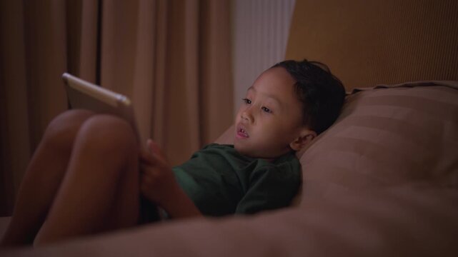 A boy lying in bed and looking at a smartphone with a smile at night, illustrating bedtime screen time, mobile gaming, and excessive phone use.