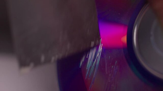 Metal blade scraping glossy circular disc with bright blue magenta reflections, fresh scratch marks, fine debris, and intense surface abrasion during active rotation