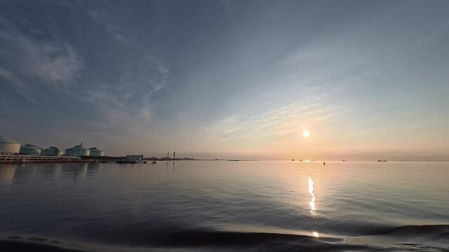 Stunning real-time video clip featuring a bright sunroad reflecting over the calm sea near a coastal factory