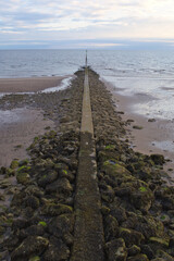 Fototapeta premium sea defences showing a concrete and rock groyne extending into the sea at low tide under a pastel evening sky.