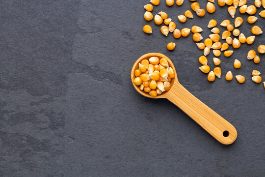 Popcorn kernels presented in a wooden spoon with scattered kernels, ideal for cooking and food concepts