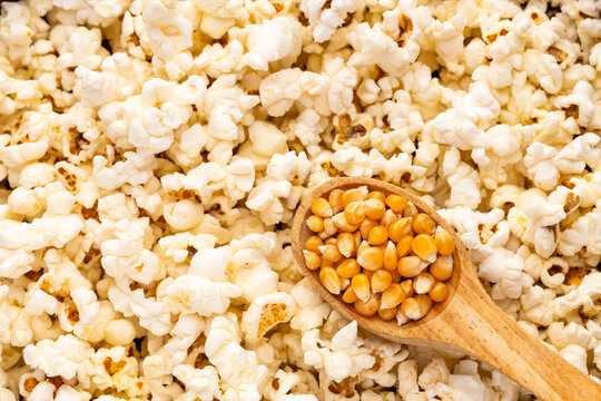 Wooden spoon with popcorn kernels next to popped popcorn