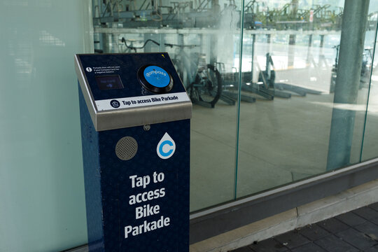 A Compass Card reader kiosk reading Tap to access Bike Parkade stands at the glass entrance to a secure TransLink bicycle parkade at a transit station.