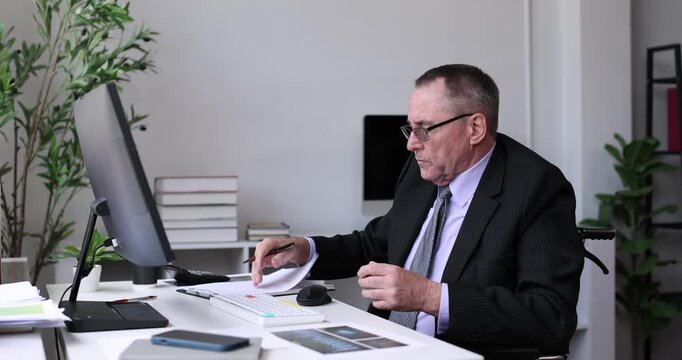 Man in wheelchair diligently analyzing digital business charts and data on a desktop computer, representing an inclusive and accessible work environment for employees with disabilities
