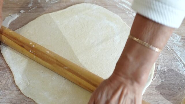Traditional cooking process showing hands rolling thin dough with wooden rolling pin on a floured surface for homemade food preparation