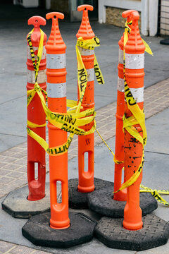 Orange traffic delineator posts wrapped in yellow caution tape on a city sidewalk. Construction zone safety barrier, roadwork warning signal, urban security, maintenance or hazard block.