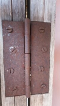 Close-up of an old, heavily rusted metal door hinge with screws attached to weathered wood.