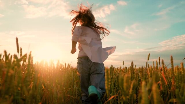 Kid girl playing runs wheat field in countryside. Happy child running merrily field. Kid girl dreams plays in countryside. Child dreams, child fantasy. Child runs in nature. Family vacations in nature