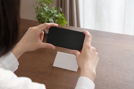 スマートフォンで無地カードを撮影する女性の手元