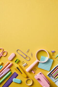 High angle view of pastel school supplies organized at the bottom of a vertical yellow background with copy space