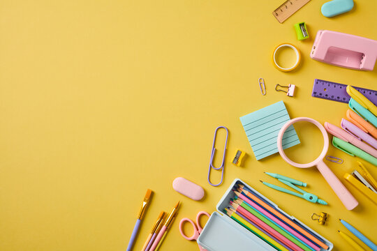 School stationery in pastel colors arranged on the right side of a yellow background with large empty copy space on the left.